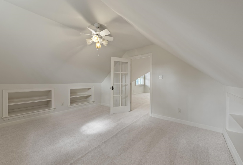 Bonus room with built in shelves, ceiling fan, and light carpet