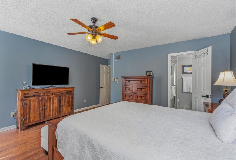 Bedroom with a textured ceiling, a ceiling fan, wood finished floors, and connected bathroom