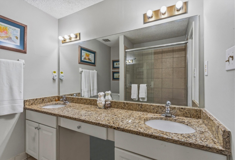 Bathroom featuring double vanity, a textured ceiling, and a shower stall