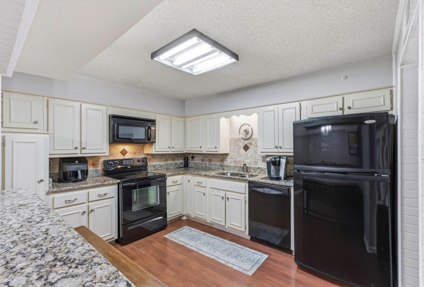 Kitchen with black appliances, backsplash, dark wood-type flooring, and a textured ceiling