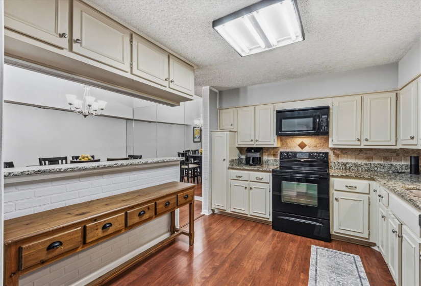 Kitchen with black appliances, a textured ceiling, dark wood-style floors, cream cabinetry, and backsplash