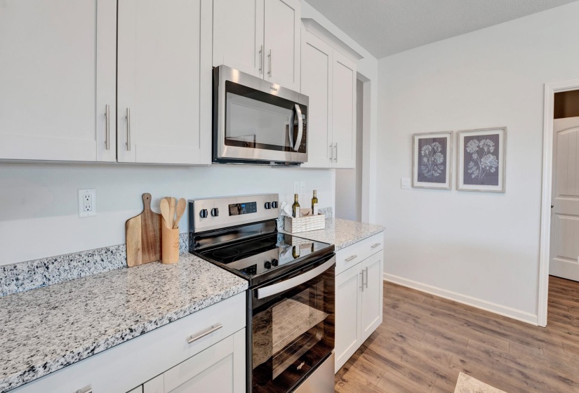 Kitchen with stainless steel appliances, light wood-type flooring, white cabinets, and light stone counters