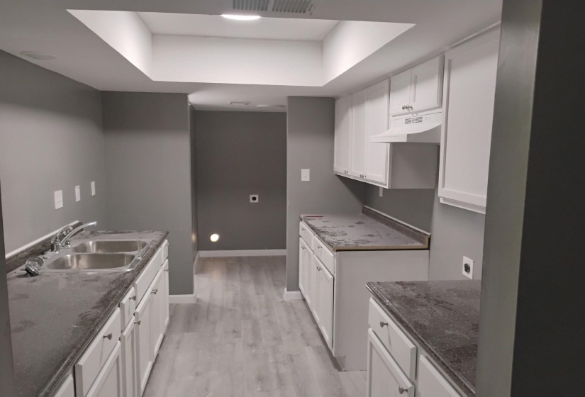 Kitchen with white cabinets, a raised ceiling, light wood-type flooring, and under cabinet range hood