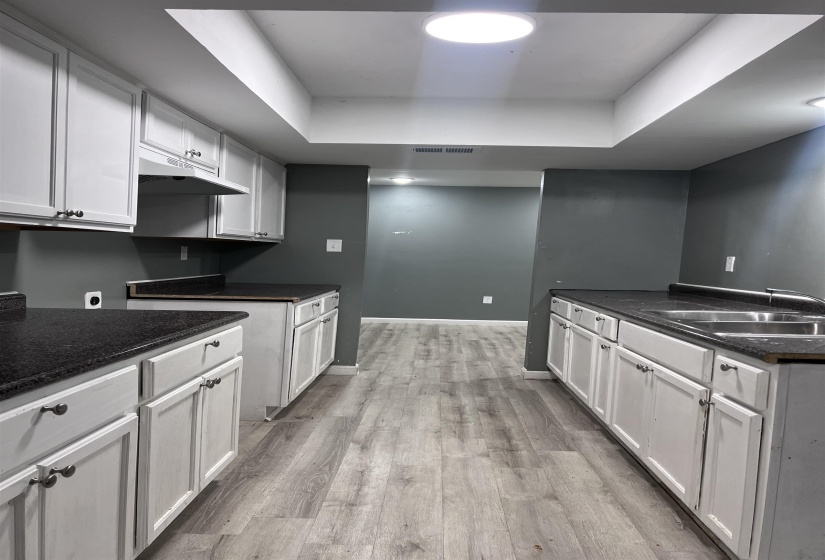 Kitchen with a tray ceiling, light wood-type flooring, white cabinets, and under cabinet range hood