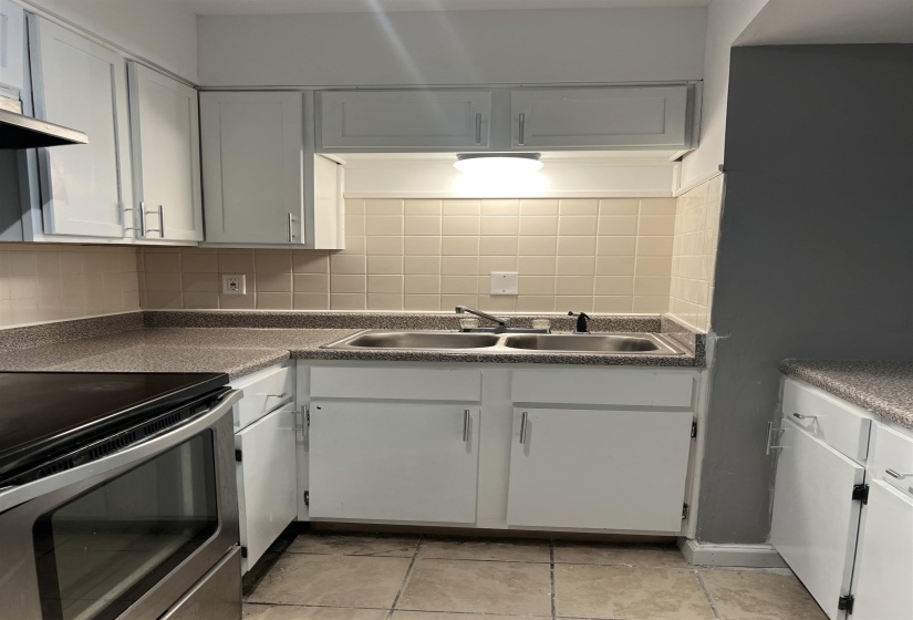 Kitchen with stainless steel range with electric cooktop, tasteful backsplash, white cabinets, and light tile patterned flooring