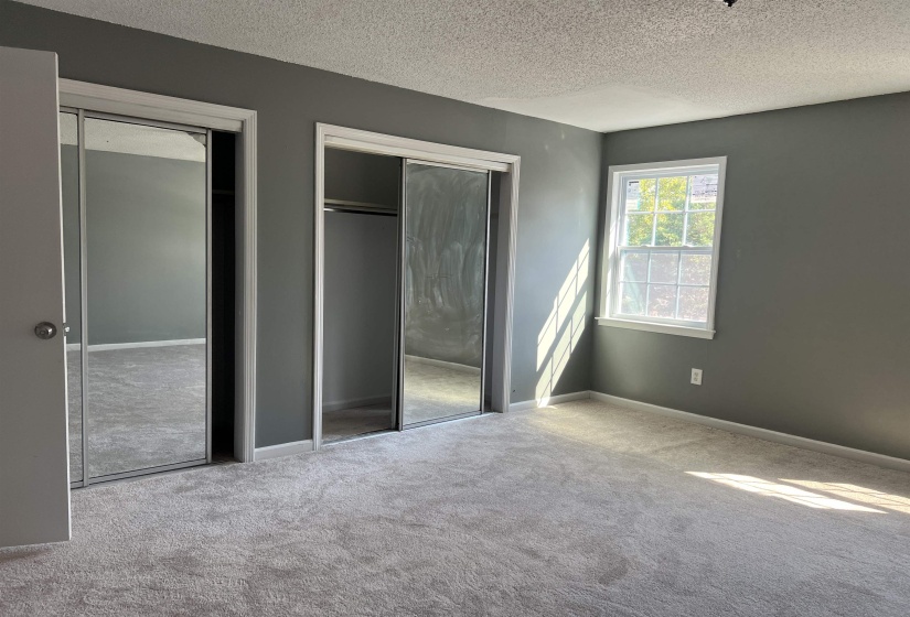 Unfurnished bedroom with two closets, a textured ceiling, and carpet floors