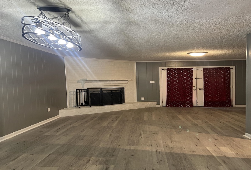 Unfurnished living room with a fireplace, hardwood / wood-style floors, wood walls, ornamental molding, and a textured ceiling