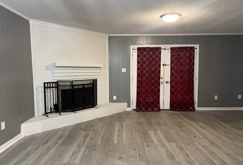 Unfurnished living room featuring ornamental molding, wooden walls, a textured ceiling, wood finished floors, and a brick fireplace