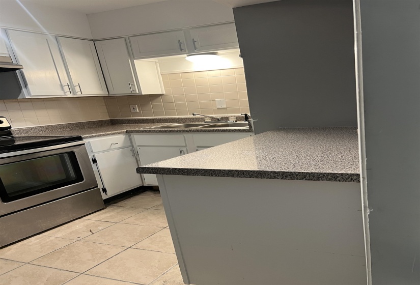 Kitchen featuring stainless steel range with electric stovetop, backsplash, white cabinetry, light tile patterned floors, and dark countertops