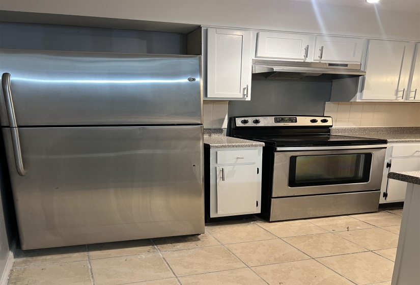 Kitchen featuring stainless steel appliances, white cabinets, under cabinet range hood, and backsplash