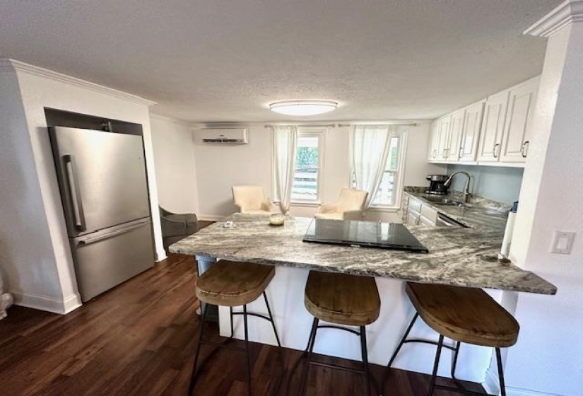 Kitchen with a wall unit AC, dark hardwood / wood-style flooring, white cabinets, light stone countertops, and stainless steel fridge