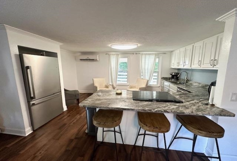 Kitchen featuring a kitchen bar, light stone counters, white cabinets, stainless steel fridge, and dark wood-type flooring