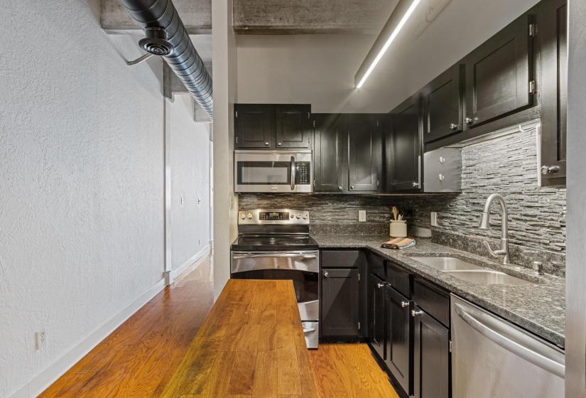 Kitchen featuring stainless steel appliances, tasteful backsplash, a textured wall, dark cabinets, and light wood-style floors