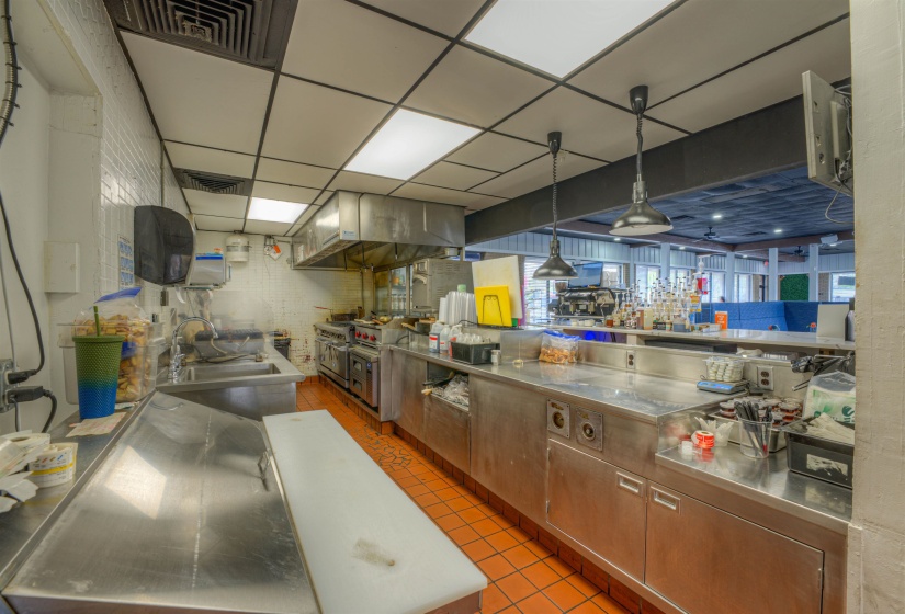 Kitchen with stainless steel countertops, decorative light fixtures, a paneled ceiling, range hood, and wood finish cabinets