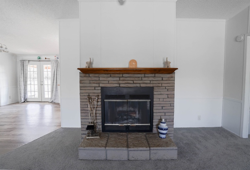Detailed view of a textured ceiling, a brick fireplace, french doors, and carpet floors