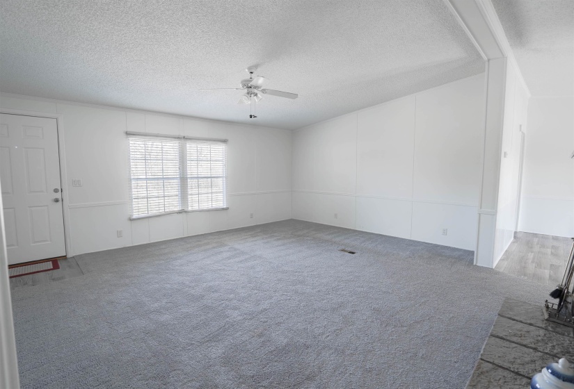 Unfurnished living room featuring carpet, a ceiling fan, and a textured ceiling