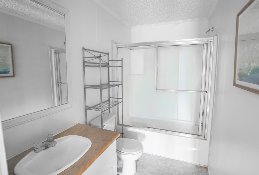 Bathroom with a textured ceiling, enclosed tub / shower combo, and vanity