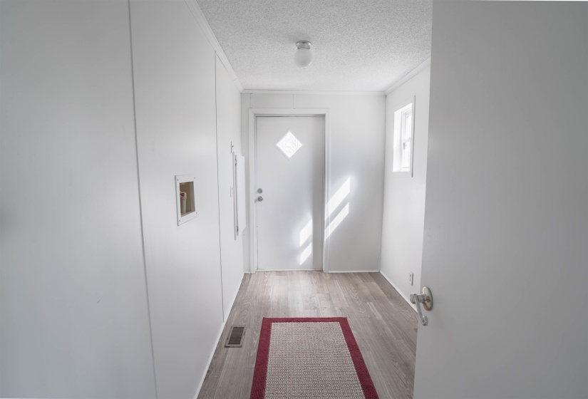 Doorway with crown molding, wood finished floors, and a textured ceiling