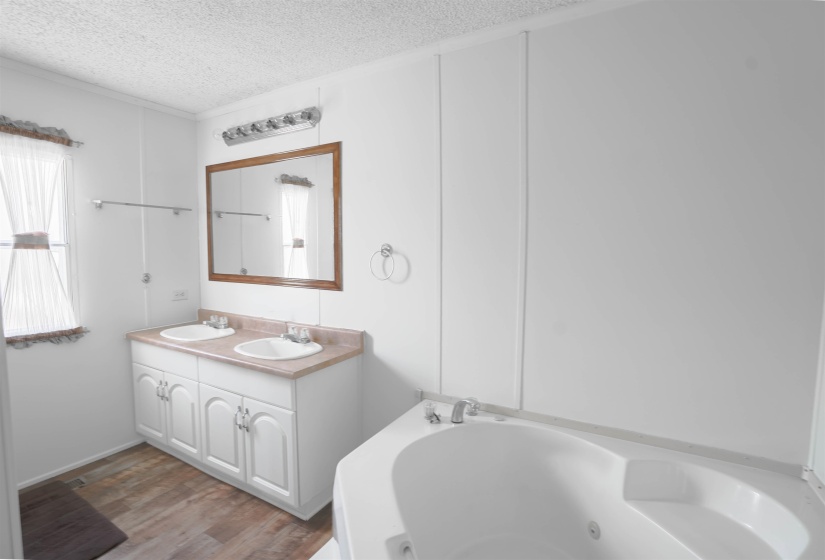 Bathroom featuring double vanity, wood finished floors, a textured ceiling, and a whirlpool tub