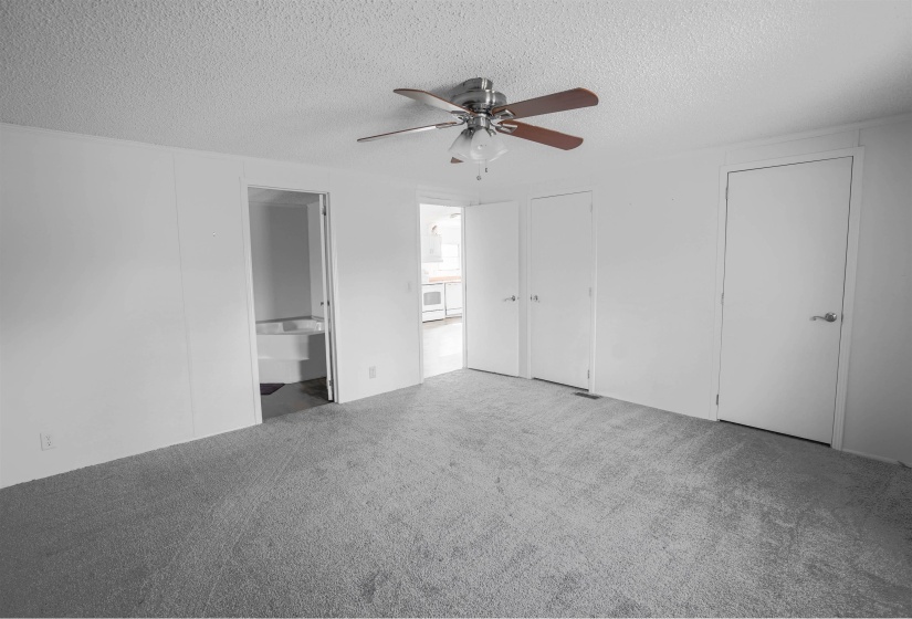 Unfurnished bedroom featuring a textured ceiling, two closets, carpet, ceiling fan, and ensuite bathroom