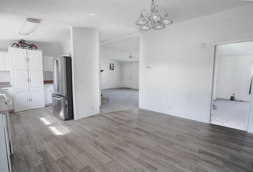 Unfurnished dining area featuring ceiling fan, a textured ceiling, light wood finished floors, light colored carpet, and hanging lights
