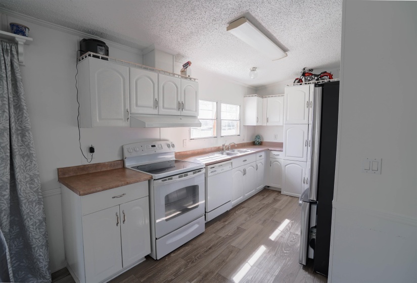 Kitchen featuring white appliances, a textured ceiling, white cabinets, light wood-style flooring, and ornamental molding