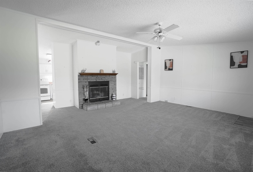 Unfurnished living room with a textured ceiling, carpet floors, a ceiling fan, and a brick fireplace