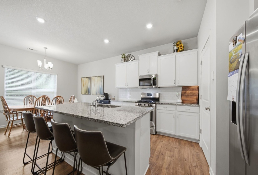Kitchen with stainless steel appliances, white cabinetry, light stone countertops, a center island with sink, and a breakfast bar