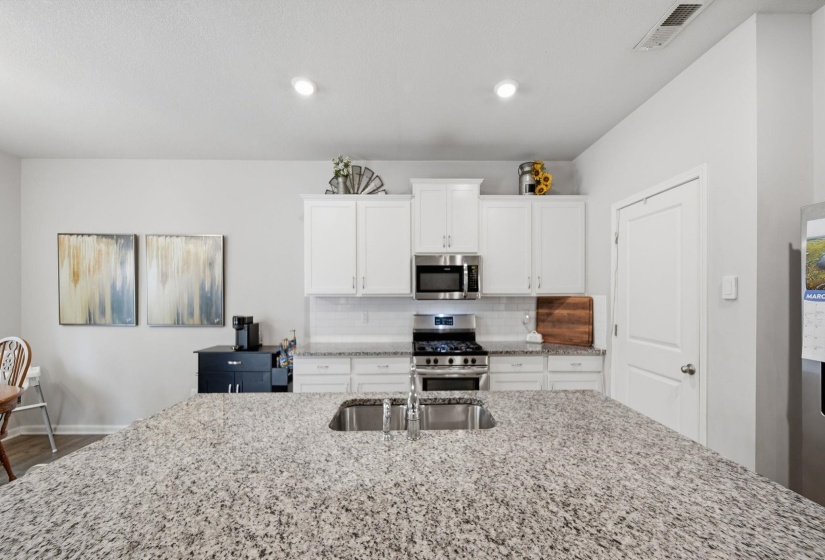 Kitchen with stainless steel appliances, light stone counters, decorative backsplash, white cabinetry, and an island with sink
