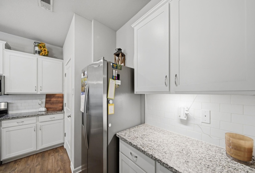Kitchen with tasteful backsplash, light stone counters, stainless steel appliances, and white cabinetry