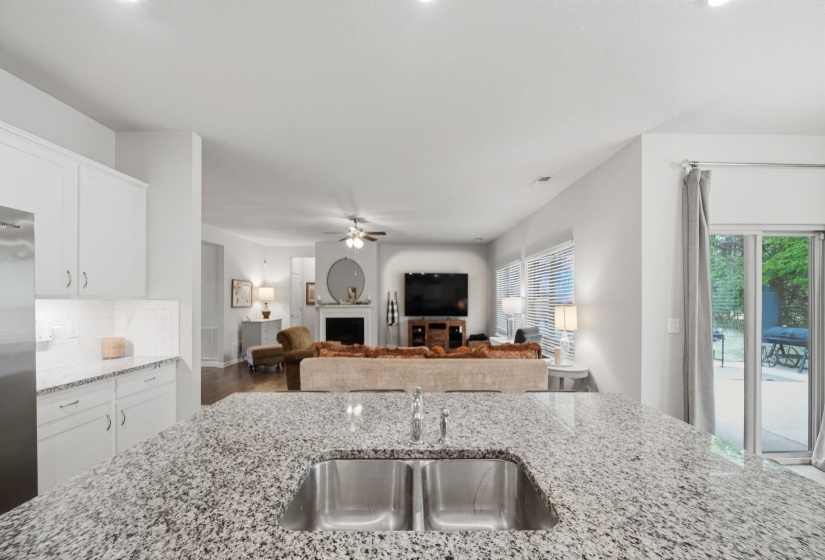 Kitchen featuring open floor plan, a fireplace, light stone countertops, a ceiling fan, and stainless steel refrigerator