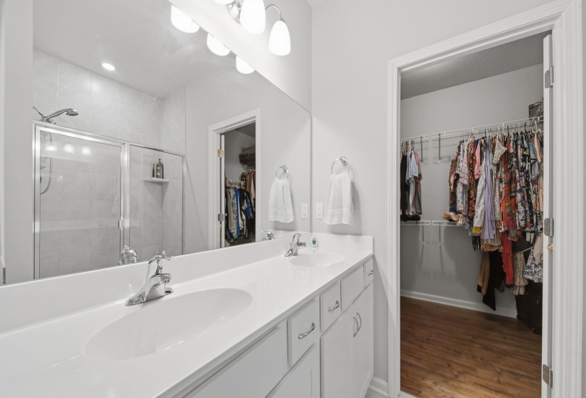 Full bath with double vanity, a stall shower, wood finished floors, a walk in closet, and recessed lighting