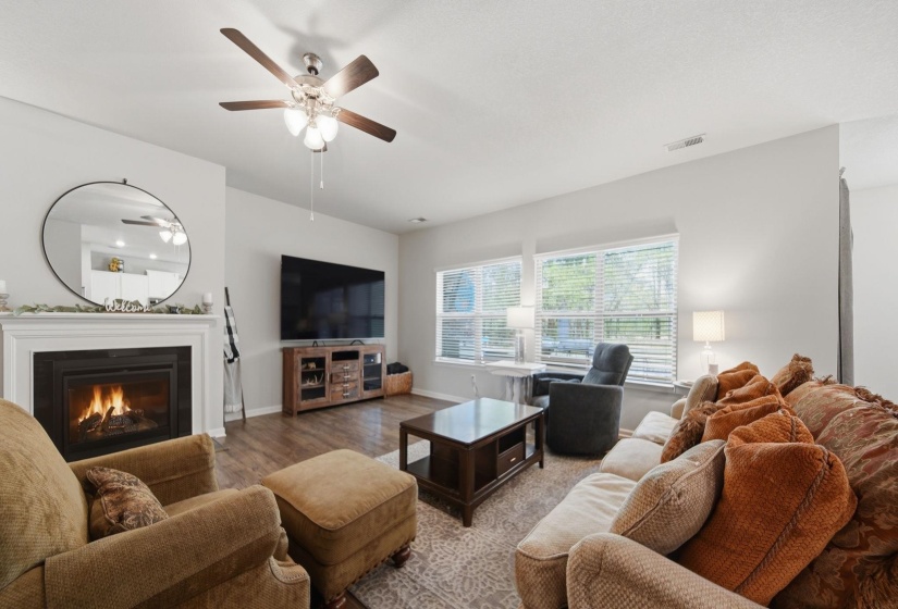 Living room with a glass covered fireplace, wood finished floors, and ceiling fan