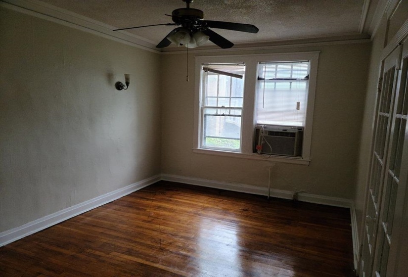 Empty room featuring dark wood-type flooring, a textured ceiling, a ceiling fan, ornamental molding, and cooling unit
