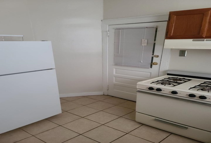 Kitchen with white appliances, light tile patterned floors, under cabinet range hood, and brown cabinetry