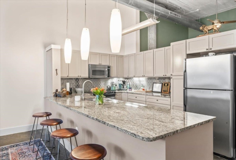 Kitchen with a breakfast bar area, stainless steel appliances, decorative light fixtures, a high ceiling, and light stone countertops