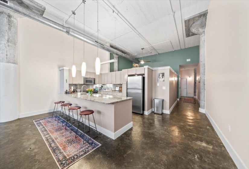 Kitchen with finished concrete floors, stainless steel appliances, light stone counters, a high ceiling, and a kitchen breakfast bar