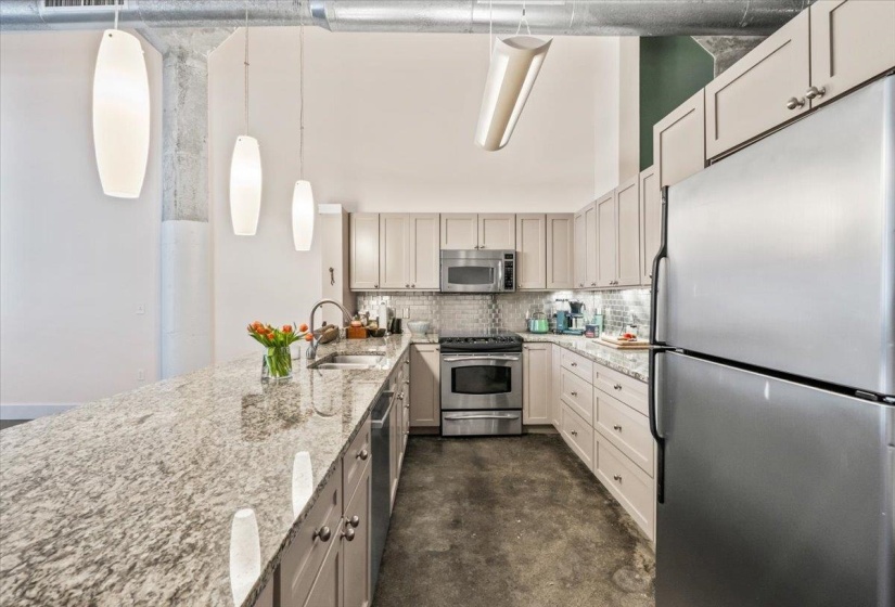 Kitchen featuring stainless steel appliances, light stone counters, backsplash, pendant lighting, and concrete floors