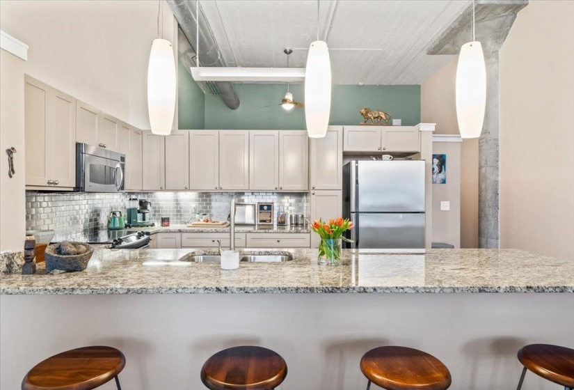 Kitchen featuring a kitchen breakfast bar, stainless steel appliances, light stone countertops, a peninsula, and tasteful backsplash