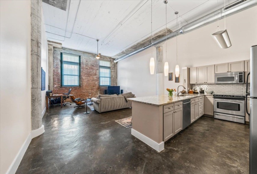 Kitchen with brick wall, a peninsula, stainless steel appliances, finished concrete floors, and open floor plan