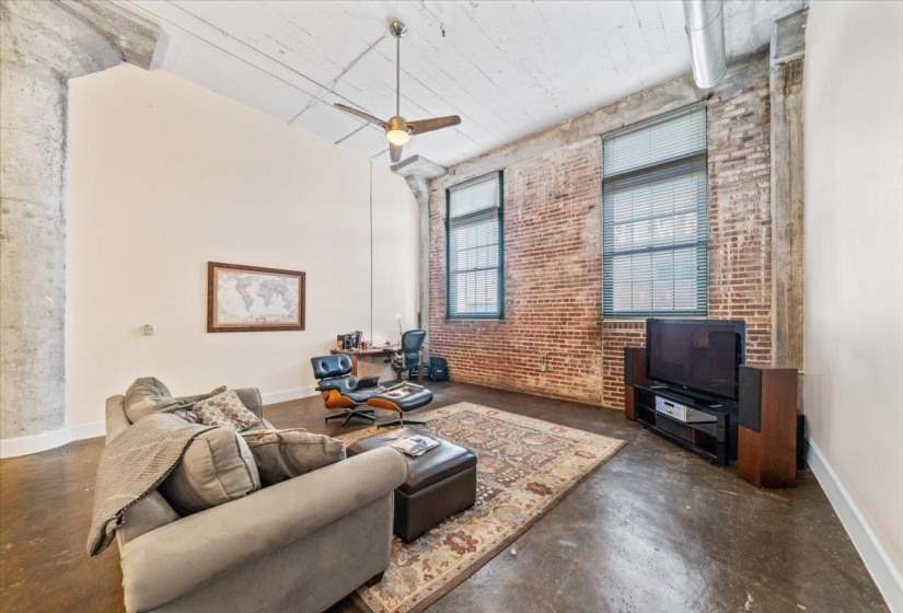 Living room featuring brick wall, finished concrete flooring, a ceiling fan, and a high ceiling