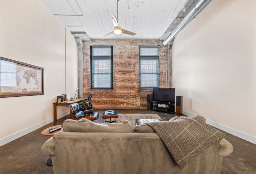 Living area with brick wall, concrete floors, and ceiling fan
