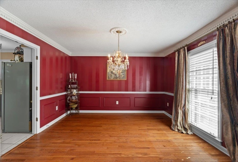 Unfurnished dining area featuring a chandelier, a textured ceiling, light wood-style flooring, crown molding, and a decorative wall