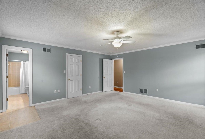 Unfurnished bedroom featuring light carpet, a textured ceiling, crown molding, and a ceiling fan