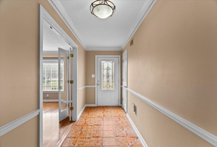 Doorway with ornamental molding, a textured ceiling, and tile patterned flooring