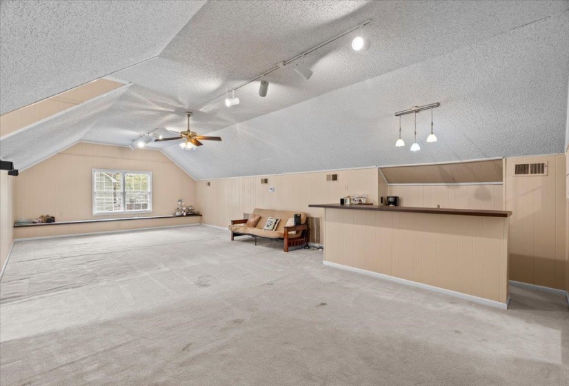 Additional living space featuring wooden walls, light carpet, a textured ceiling, and ceiling fan