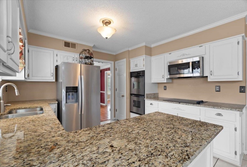 Kitchen with stainless steel appliances, crown molding, light stone countertops, white cabinets, and a textured ceiling