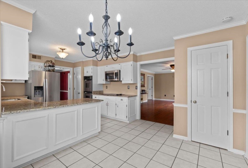 Kitchen featuring ornamental molding, white cabinets, stainless steel appliances, light stone countertops, and suspended lighting