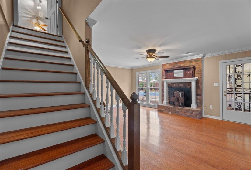 Stairway with a ceiling fan, crown molding, a fireplace, and wood finished floors