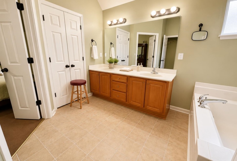 Bathroom featuring a double vanity with light wood cabinetry, a built-in bathtub, and large square floor tiles